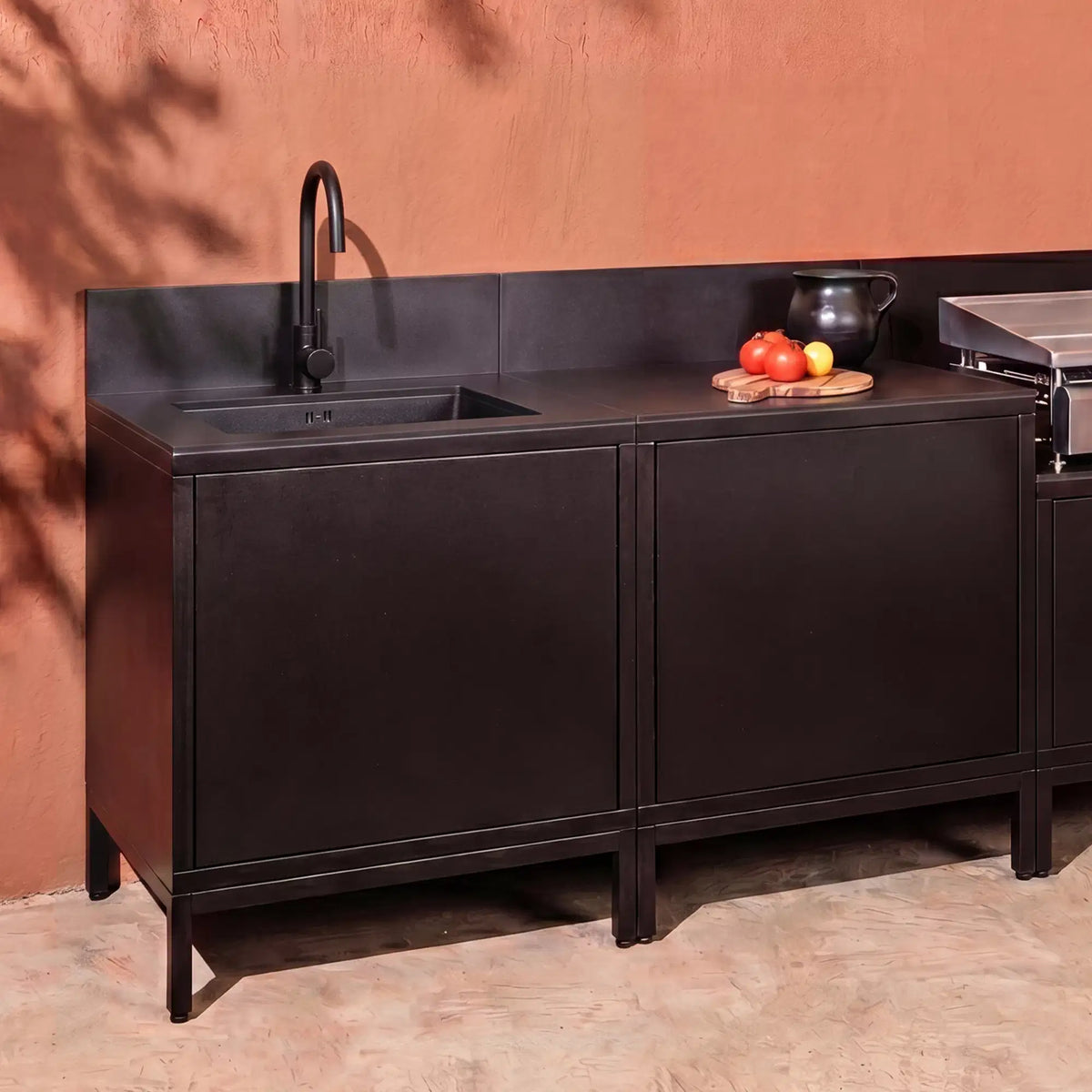 Cocina exterior Pilotis en negro intenso con módulo de fregadero, encimera de cerámica negra y plancha
::visuel:noir