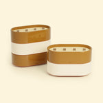 Bougies Totem L Brun terre de sienne – Citronnelle & Fleur d’oranger et Beige ivoire – Citronnelle & Citron, deux grandes bougies ovales à triple mèche en bois, posées sur un fond beige clair.