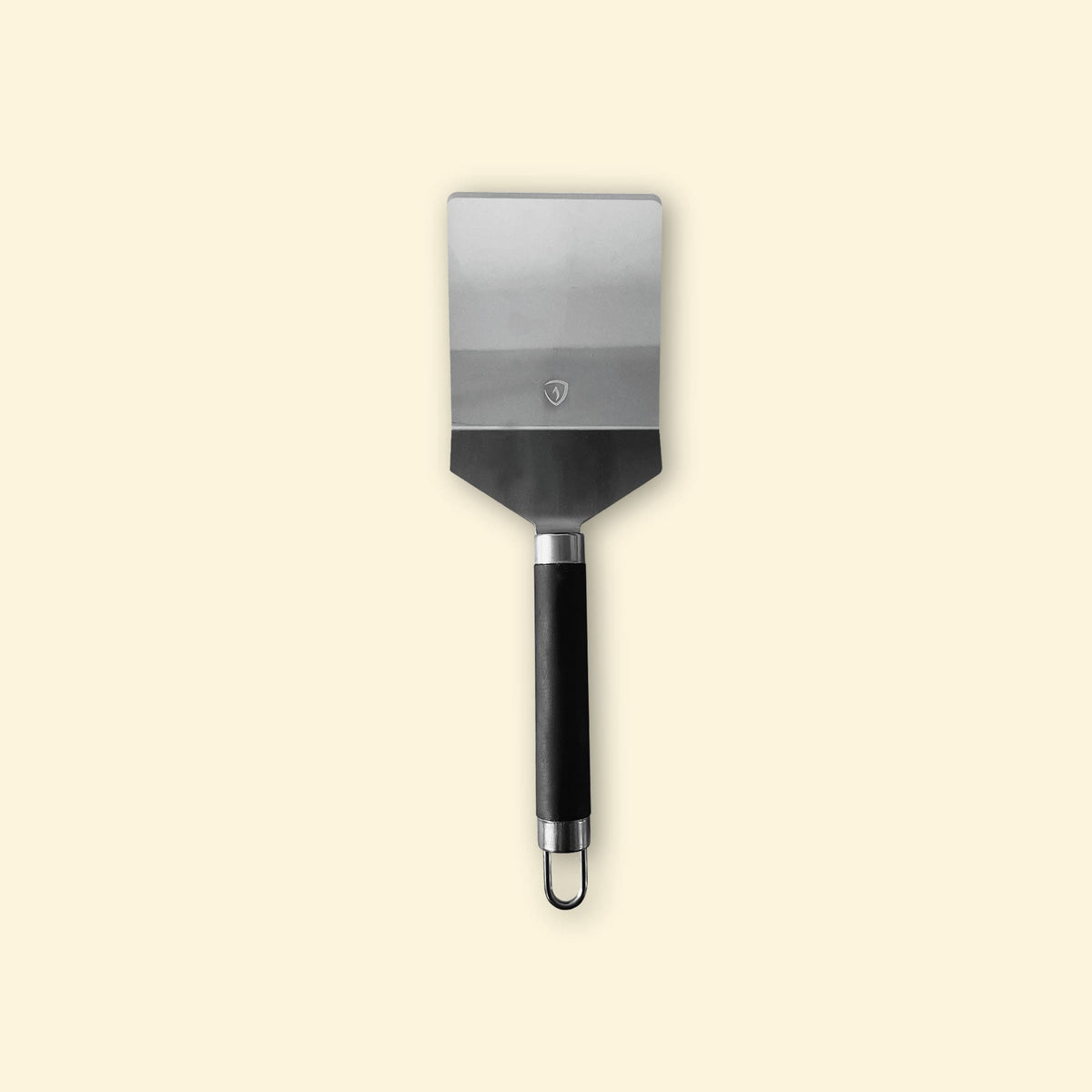 Spatule de cuisine en inox avec manche noir, vue de face sur fond beige clair.