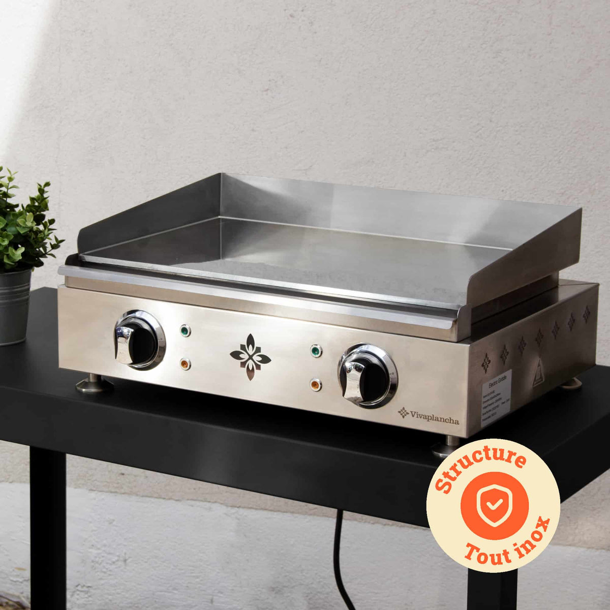 Plancha Vivaplancha colocada sobre una mesa exterior, con su estructura completamente de acero inoxidable destacada y una insignia “Estructura todo en inox” mostrada en un círculo naranja.